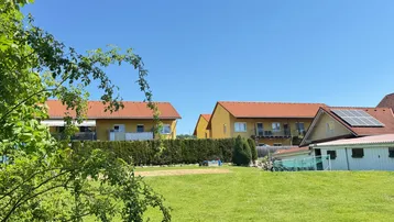 Wohngebäude mit roten Dächern und Solaranlage, umgeben von grüner Natur und Bäumen.