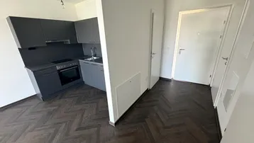 Offene Küchenzeile mit dunklen Schränken und Fischgrätparkett im Eingangsbereich der Wohnung.
