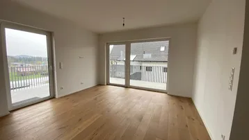 Geräumiger Wohnbereich mit großen Fenstern und Balkonzugang, der eine weite Aussicht bietet.