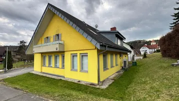 Seitenansicht des gelben Gebäudes mit Rasenfläche und Dachfenstern.