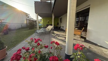 Sonnige Terrasse mit Liegestühlen und blühenden Rosen, angrenzend an einen gepflegten Rasenbereich.
