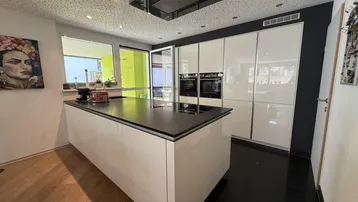 Moderne offene Küche mit weißer Hochglanzfront, Kücheninsel und integrierten Geräten.