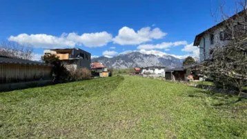 Weitläufige grüne Wiese mit Blick auf schneebedeckte Berge unter blauem Himmel.