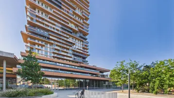Modernes Hochhaus mit vielen Balkonen und Glasfassade in urbaner Umgebung.