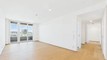 Helles, leeres Wohnzimmer mit Parkettboden und Zugang zu einem Balkon mit Stadtblick.