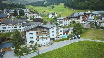Eine Luftaufnahme des Hotels in einer bergigen Landschaft mit umliegenden Häusern und viel Grün.
