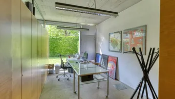 Helles Büro mit großen Fenstern, Blick ins Grüne und praktischen Holzschränken, ideal für konzentriertes Arbeiten.
