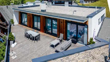 Große Dachterrasse mit Holzbelag und modernen Gartenmöbeln, umgeben von alpiner Landschaft.