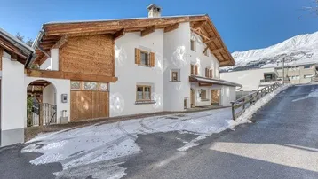 Traditionelles Haus mit Holzelementen und schneebedeckter Auffahrt in alpiner Umgebung.