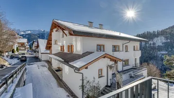 Sonnenbeschienenes Chalet mit schneebedecktem Dach und Blick auf die umliegende Berglandschaft.