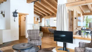 Gemütlicher Wohnbereich im alpinen Stil mit Holzbalkendecke, Kamin und offener Küche.