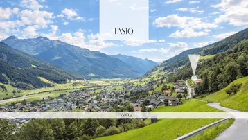 Panoramablick auf ein malerisches Tal mit einer Siedlung und majestätischen Bergen unter blauem Himmel.