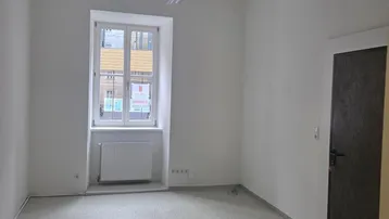 Heller, leerer Raum mit einem Fenster, das Tageslicht hereinlässt, und einem Heizkörper darunter.