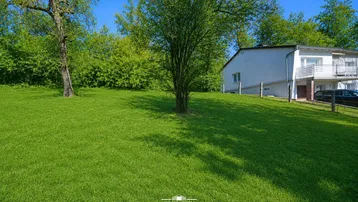 Weitläufige Grünfläche mit Baumbestand und Blick auf das Wohnhaus mit Balkon.