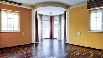 Helles Zimmer mit dunklem Parkettboden und einem runden Erkerbereich mit großen Fenstern.