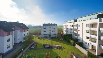 Blick auf die Wohnanlage mit gepflegter Grünfläche, Spielplatz und umliegender Natur.