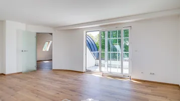 Helles, unfurniertes Zimmer mit Holzboden und Zugang zu einem Balkon durch eine Glasschiebetür.