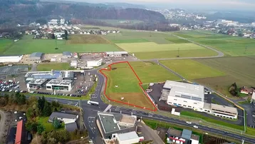 Luftaufnahme eines großen Grundstücks mit roter Umrandung, umgeben von Feldern und Gewerbegebäuden.