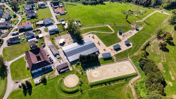 Luftaufnahme des Anwesens mit Reitplatz, Stallungen und umliegender grüner Landschaft und Bergen.