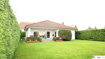 Großzügiger Gartenbereich mit Rasenfläche und überdachter Terrasse hinter dem Haus.