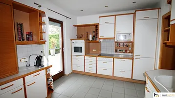 Funktionale Küche mit Holzschränken, weißen Fronten, Einbaugeräten und Zugang zum Garten.