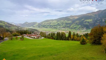 Weitläufige grüne Landschaft mit Bergen und einem Talblick, umgeben von Bäumen und Häusern.