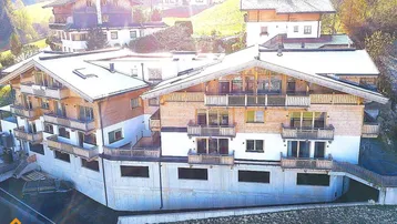 Modernes Mehrfamilienhaus im alpinen Stil mit Holzfassade und mehreren Balkonen in grüner Umgebung.