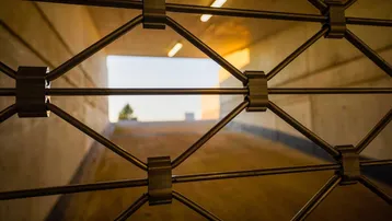 Metallgittertor vor einer Einfahrt zu einer Tiefgarage oder einem Keller mit Tageslicht am Ende.