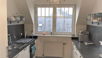 Helle Küche im Dachgeschoss mit moderner Ausstattung, Schrägdecke und Blick auf die Dächer.