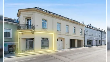 Historisches Gebäude mit heller Fassade und Balkon, das eine Gewerbefläche im Erdgeschoss hervorhebt.