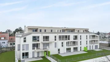 Moderne Wohnanlage mit weißer Fassade, mehreren Balkonen und grünen Rasenflächen.