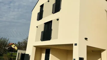 Modernes Einfamilienhaus mit heller Fassade, Satteldach und französischen Balkonen sowie überdachtem Stellplatz.