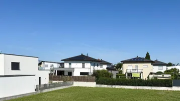 Blick auf ein grünes Baugrundstück in einer ruhigen Wohngegend mit modernen Häusern im Hintergrund.