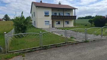 Freistehendes Haus mit Balkon, Vorgarten und Zufahrt in ländlicher Umgebung.