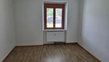 Heller, leerer Raum mit Laminatboden, weißen Wänden und einem Fenster mit Heizkörper.