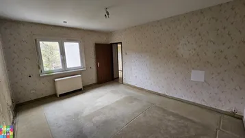 Geräumiges Zimmer mit alter Tapete und Teppichboden, das eine umfassende Renovierung benötigt.