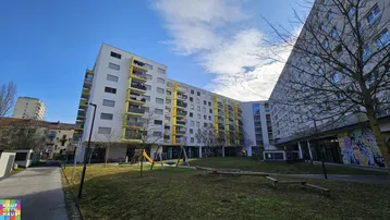 Modernes Mehrfamilienhaus mit gelben Balkonen und einem Spielplatz im begrünten Innenhof.