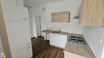 Funktionale Küchenzeile mit hellen Holz- und weißen Schränken, Spüle und Elektroherd.
