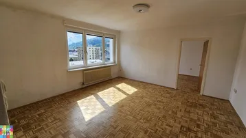 Helles Zimmer mit Parkettboden und großem Fenster, das einen weiten Blick auf die Stadt und Berge bietet.