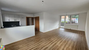Heller offener Wohnbereich mit Laminatboden und integrierter Küchenzeile, Zugang zum Balkon.