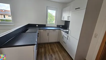 Moderne Einbauküche mit weißen Schränken, dunkler Arbeitsplatte und Fenster mit Ausblick.