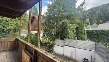 Geräumiger Holzbalkon mit Blick ins Grüne und auf die umliegende bewaldete Landschaft.