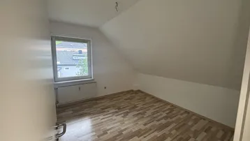 Helles Schlafzimmer mit Dachschräge, Fenster und Laminatboden, bereit zur Einrichtung.