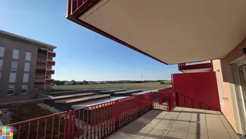 Geräumige Terrasse mit rotem Geländer und weitem Blick über die umliegende Landschaft.