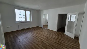 Helles, leeres Wohnzimmer mit Laminatboden und Blick auf ein gegenüberliegendes Gebäude.