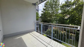 Heller Balkon mit Fliesenboden und Metallgeländer, bietet einen Blick ins Grüne.