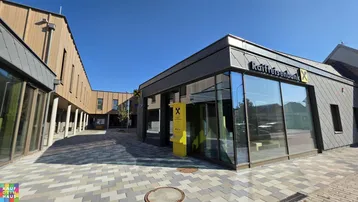 Moderne Geschäftsgebäude mit Holzfassade und großen Glasfronten, um einen gepflasterten Innenhof angeordnet.