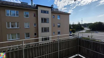 Blick vom Balkon auf die Gebäudefassade und die umliegende Straße mit Parkplätzen.