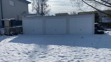 Drei weiße Garagen in einer Reihe, umgeben von einer schneebedeckten Landschaft an einem Wintertag.
