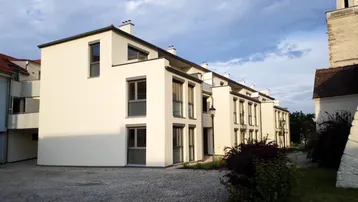 Moderne Wohngebäude mit weißer Fassade und grauen Fensterrahmen an einem gepflasterten Weg.